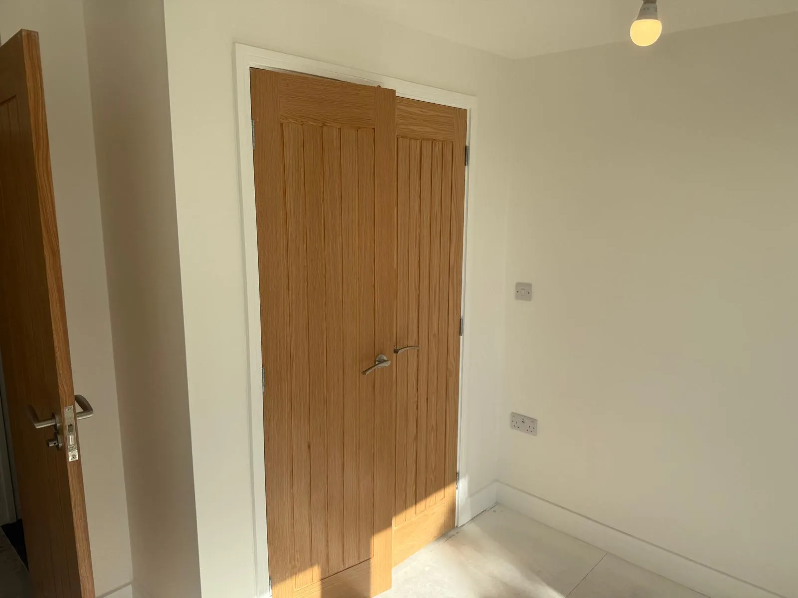 A pair of oak-veneered timber doors in a freshly painted white frame, with the hinges left clean and unpainted, in a newly redecorated room